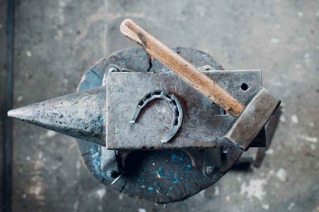 Smid met hamer en hoefijzer op metalen aambeeld, symboliserend vakmanschap in precisie metaalbewerking en plaatwalsen